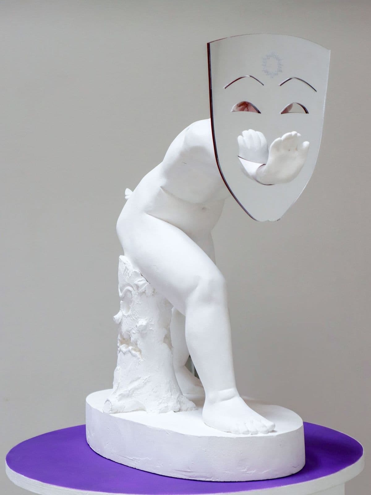 Double Act: Jokers and Sobbers, plaster sculpture by Grigorios Ilaridis of a putto reaching through a flat Greek theatre comedy mask.